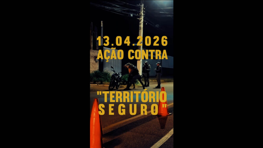 Foto mostra dois policiais à noite em uma rua mal iluminada, abordando um homem que está com as mãos na cabeça. Sobre a imagem o texto em amarelo: 13.04.2026 - Ação Contra "Território Seguro"