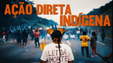 Capa do vídeo "Ação Direta Indígena" com o título em letras garrafais em laranja sobre uma fotografia de um indígena de costas, com cocar, observando à sua frente um grupo de diversos indígenas bloqueando a rodovia.